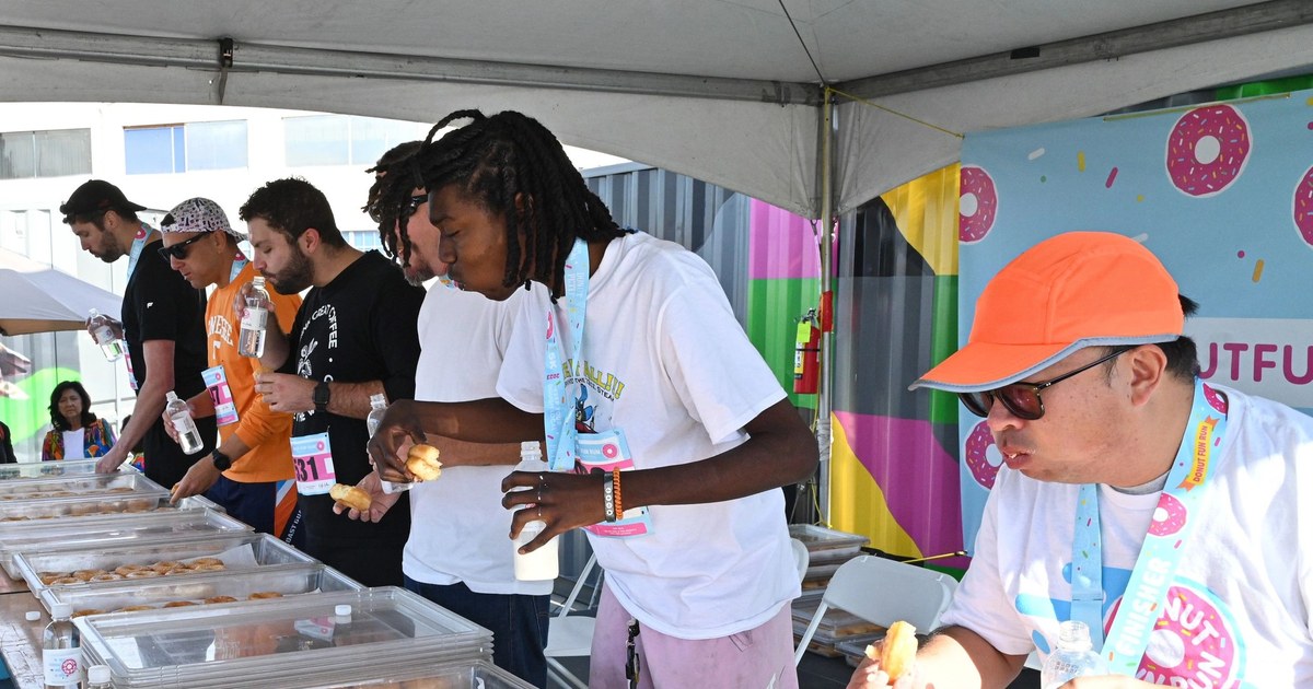 Contestants eat donuts at a long table under a tent at a previous Donut Fun Run donut eating contest. This is from an earlier race, not the 2026 event.