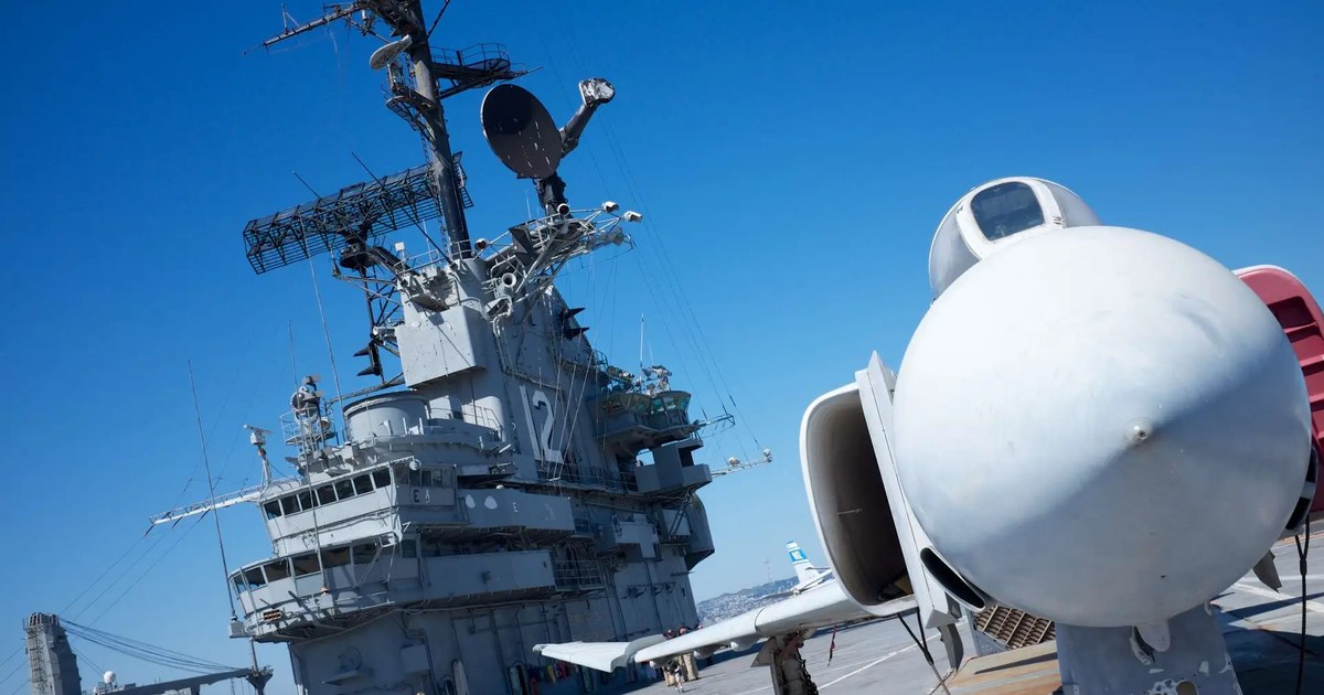 The USS Hornet aircraft carrier's tower and flight deck, docked as a museum ship in Alameda, with a parked jet in the foreground.
